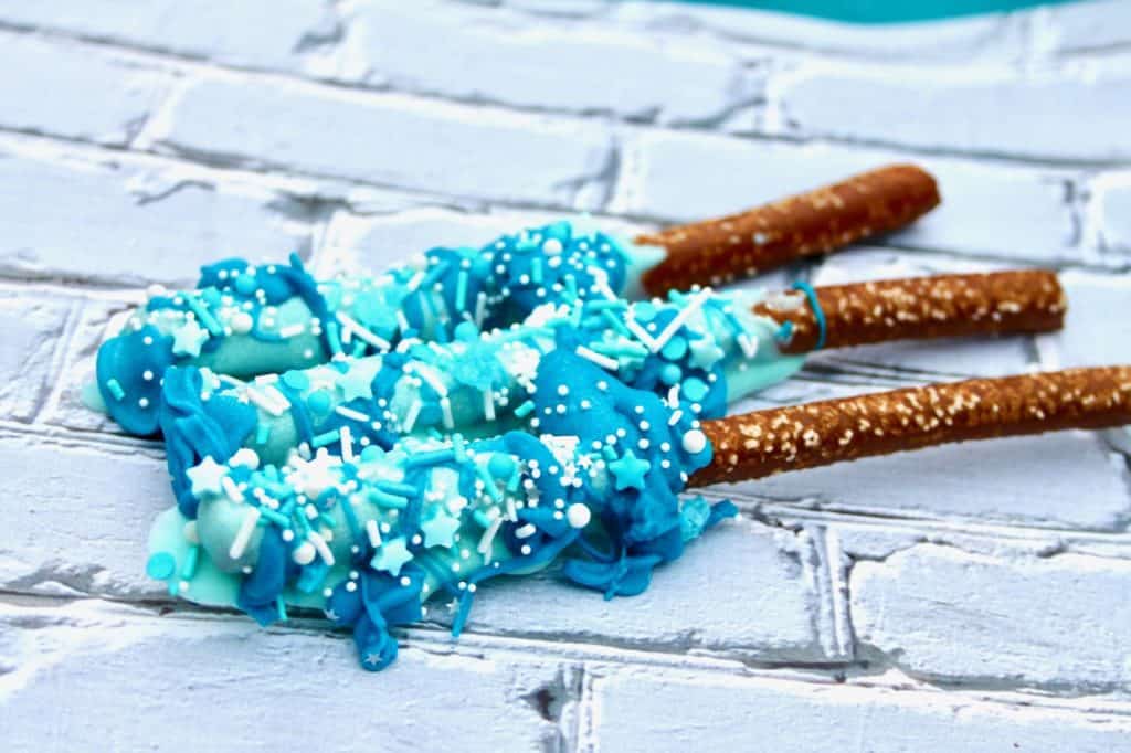 How to Make Frozen Wands (aka chocolate covered pretzel rods) Ingredients Pretzel Rods 1 cup white chocolate melting wafers divided Sprinkles (I used blue and white assorted sprinkles) food coloring (blue) Directions Melt chocolate in microwave according to package directions. Divide the mixture into 2 separate cups and add food coloring to each. ( 1 drop blue for light blue, 2 drops for dark blue) Dip the pretzel rod sticks into the light blue melted chocolate, turning to ensure coverage. Drip the dark blue melted chocolate over the blue chocolate. Place on wax paper and decorate with sprinkles. Let dry.