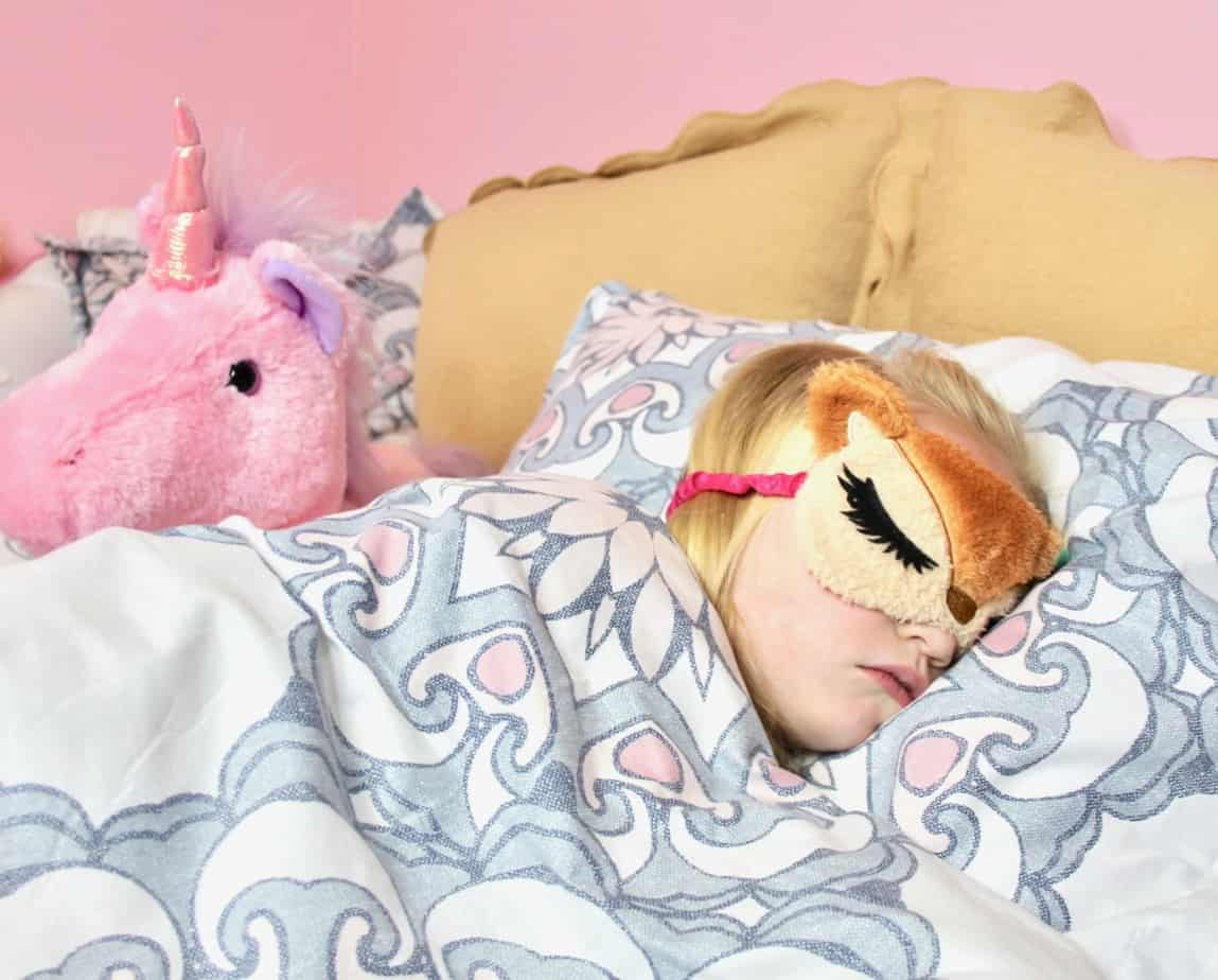 girl sleeping in bed with sleep mask and unicorn